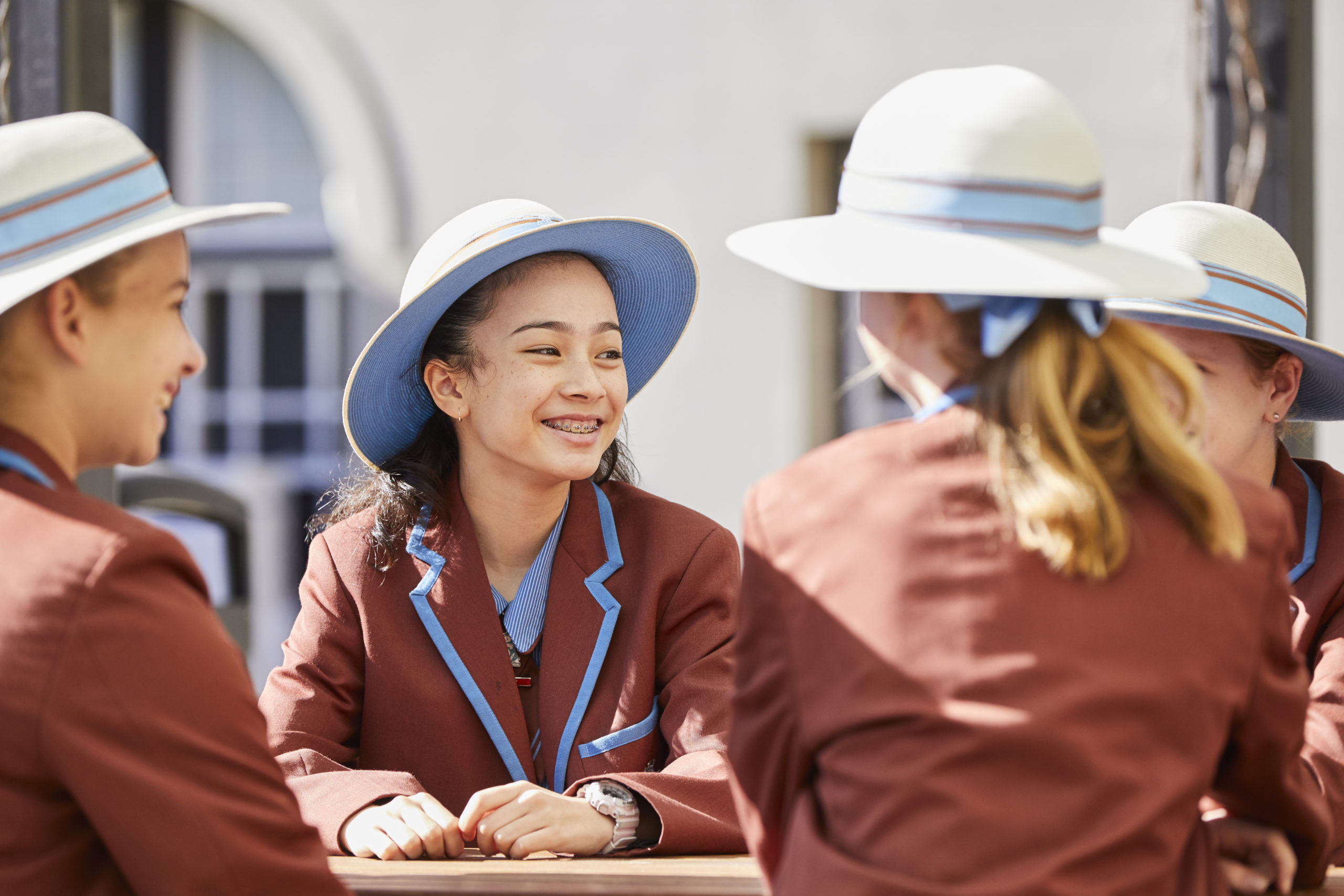 A photo of a group of All Hallows' School students sitting around a table. The photo focuses on one student who has a big smile on her face.
