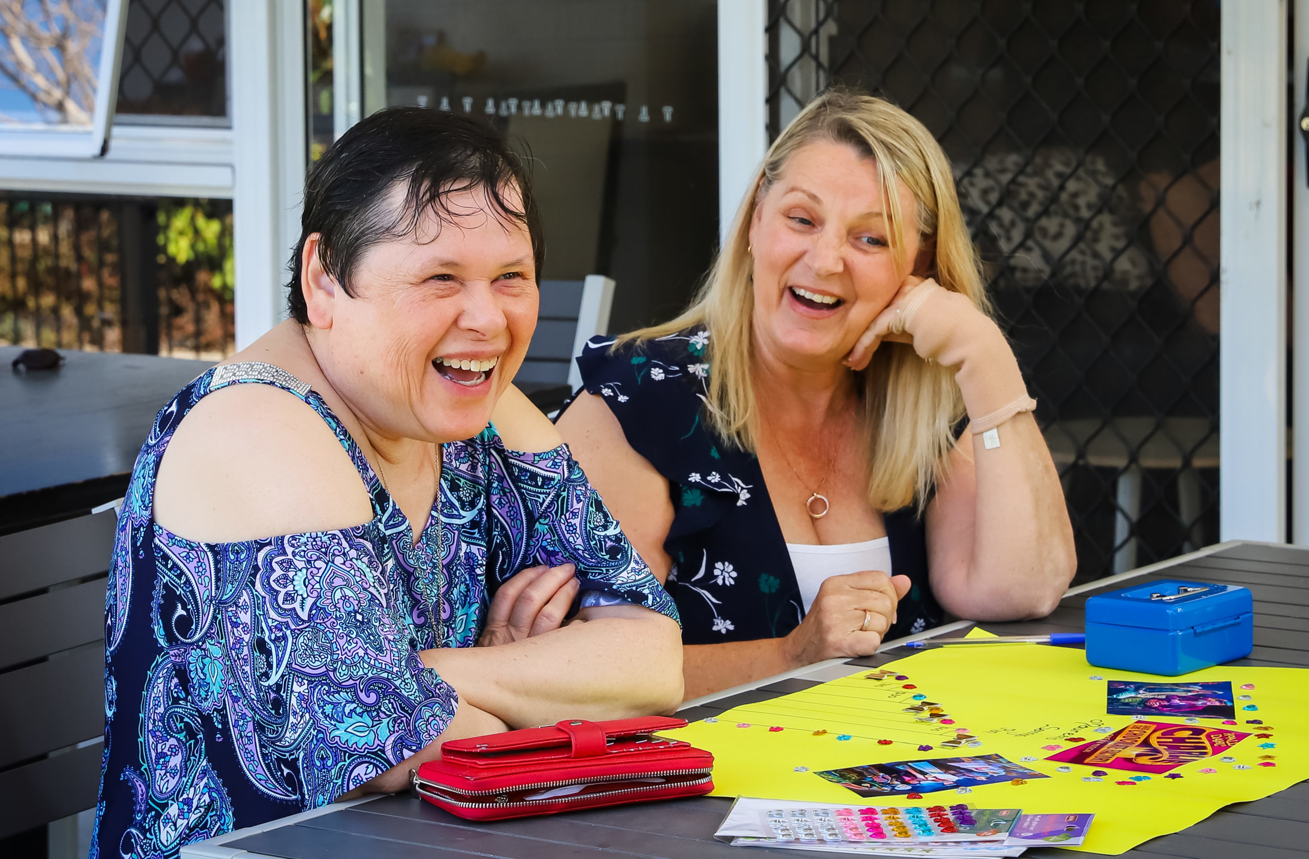 A client with a staff member enjoying a laugh, whilst creating a colour poster of photos and stickers.