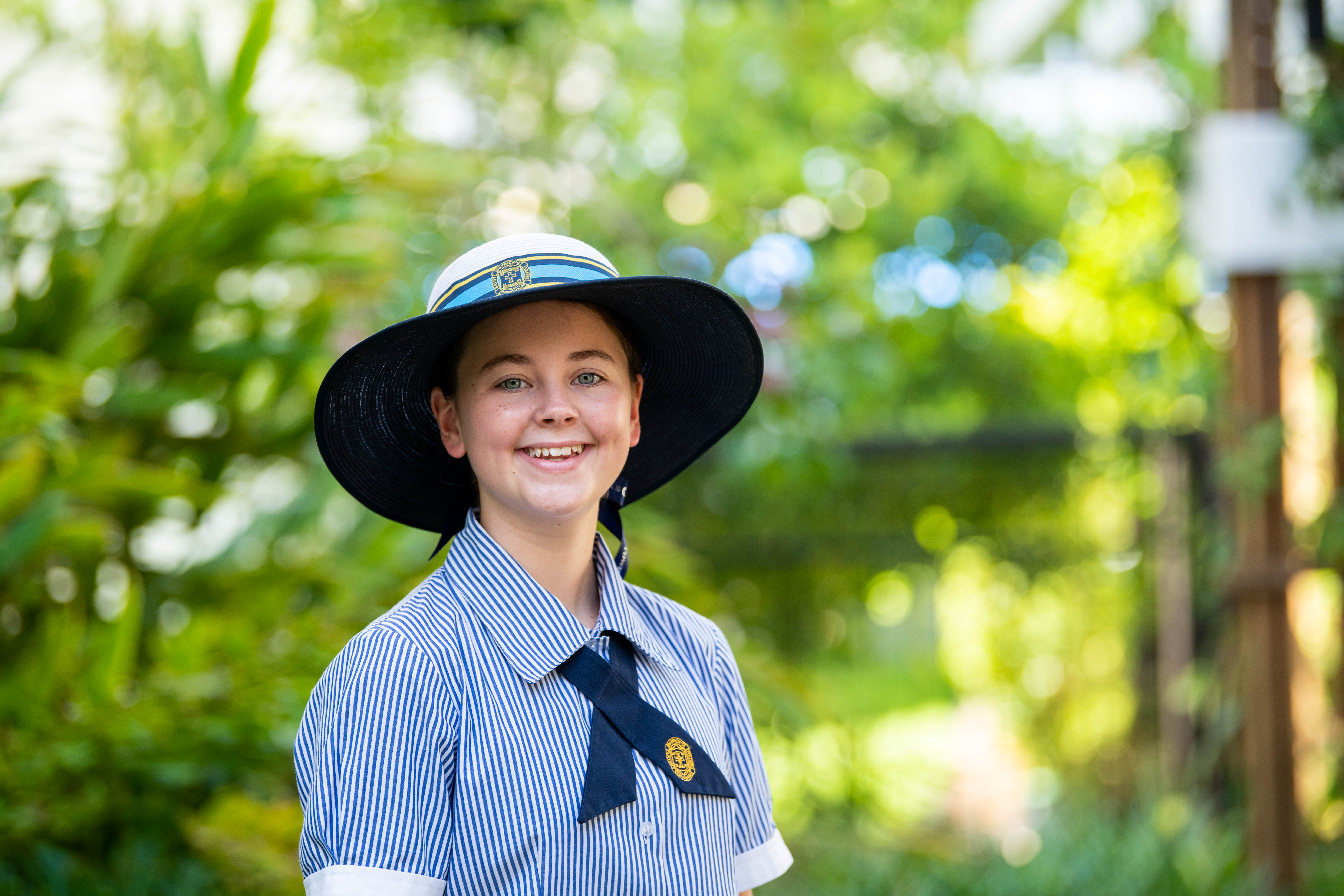 A student from St Patrick's smiling outside surrounded by lush, green trees.