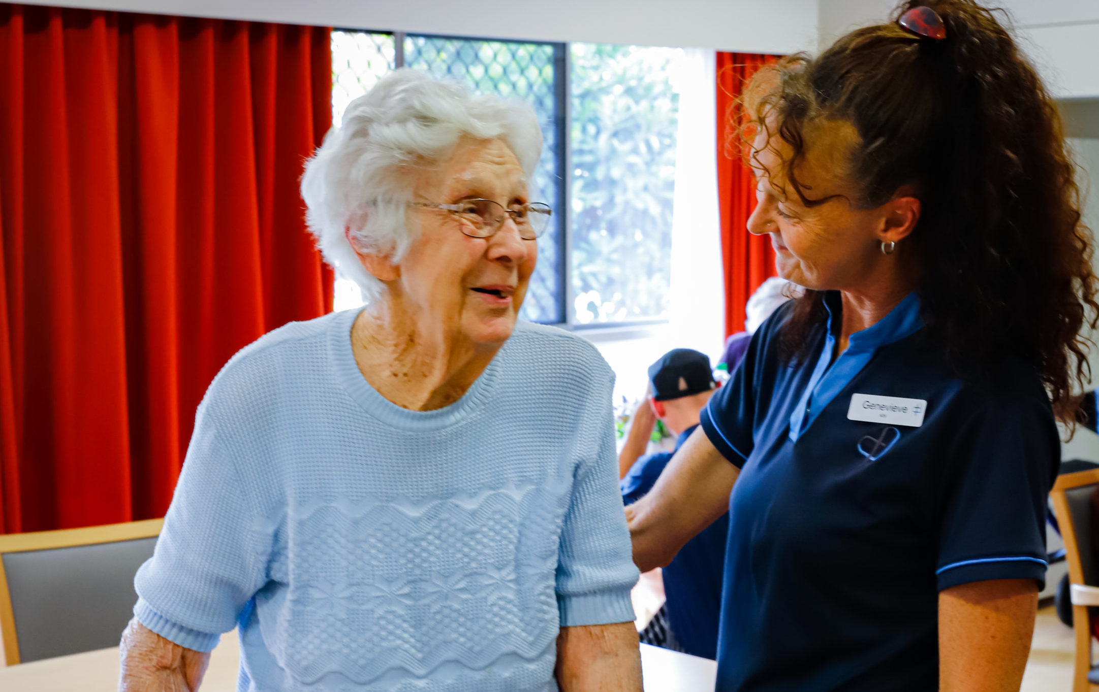 An elderly woman smiling at a friendly staff member.