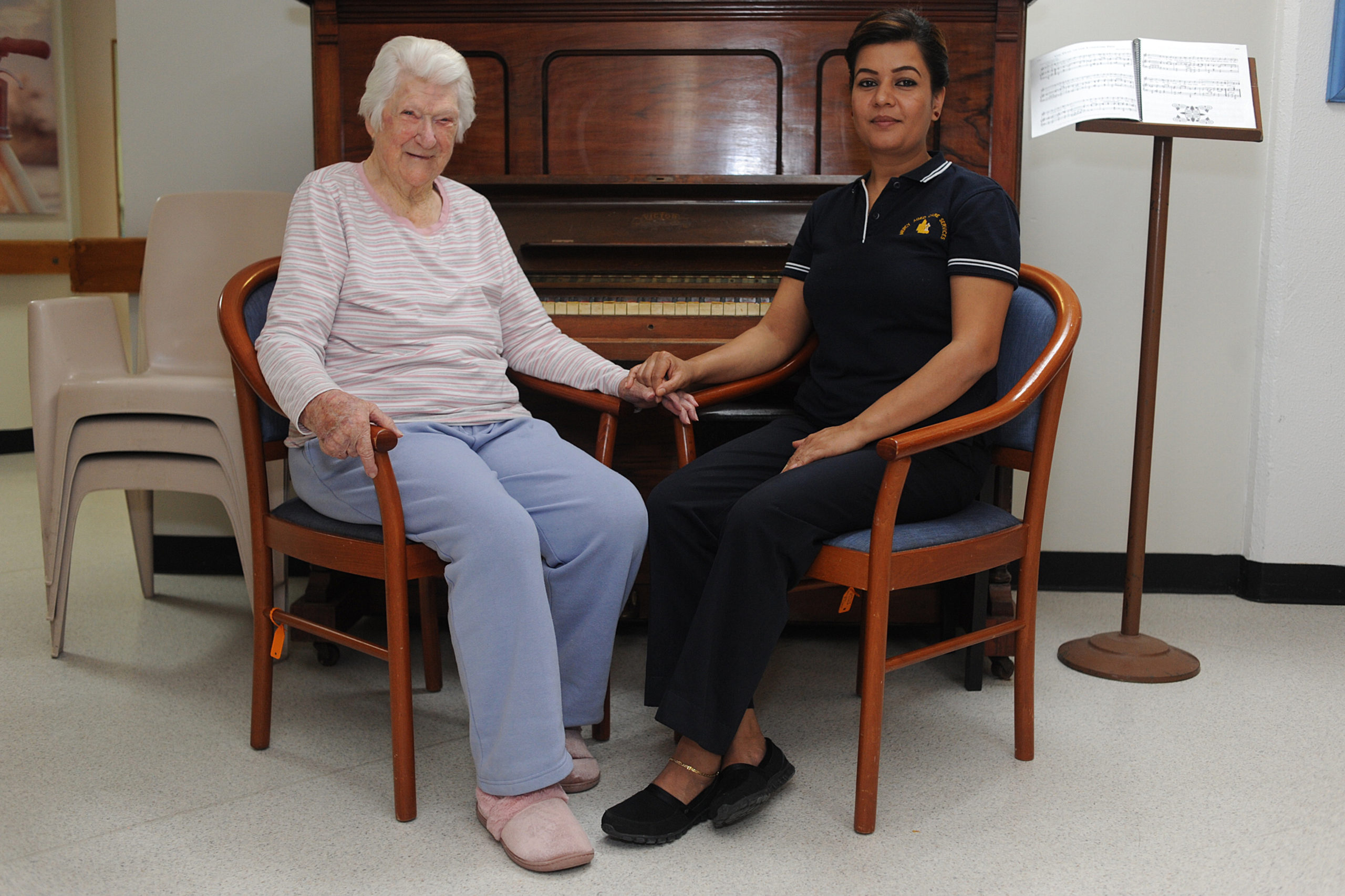 Mercy Health and Aged Care resident and member of staff holding hands and sitting closely together in front of a piano.