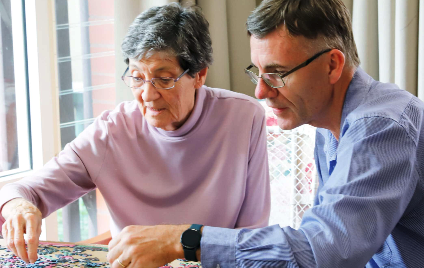 An elderly lady and a man working on a jigsaw together.