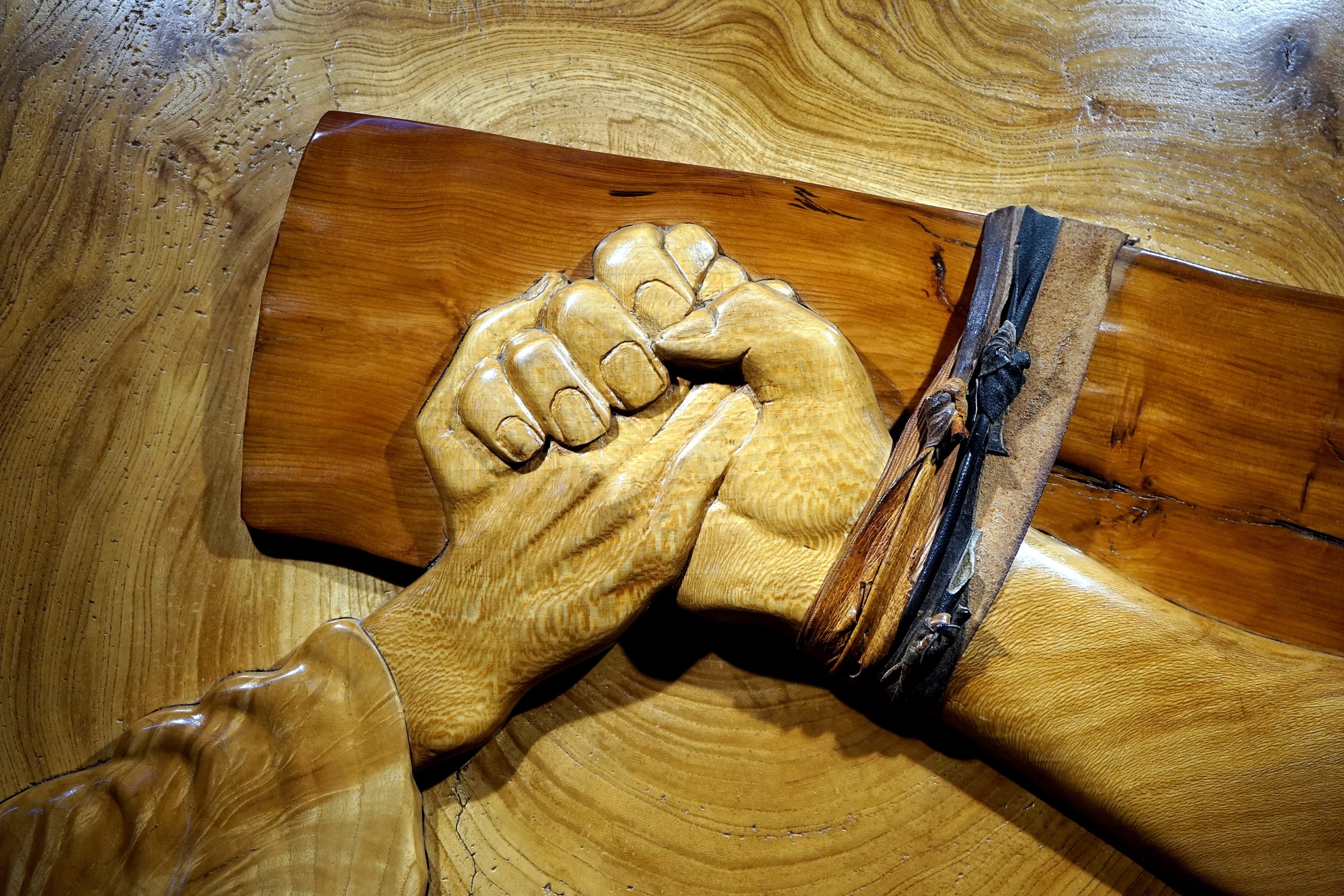 A wooden sculpture depicting a hand holding Jesus' hand on the cross.