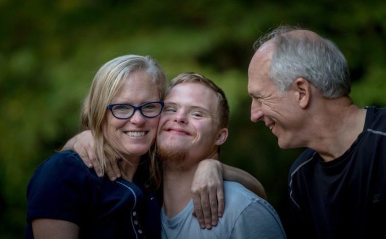 A photograph of three smiling people - a young man being embraced by a middle aged man and woman