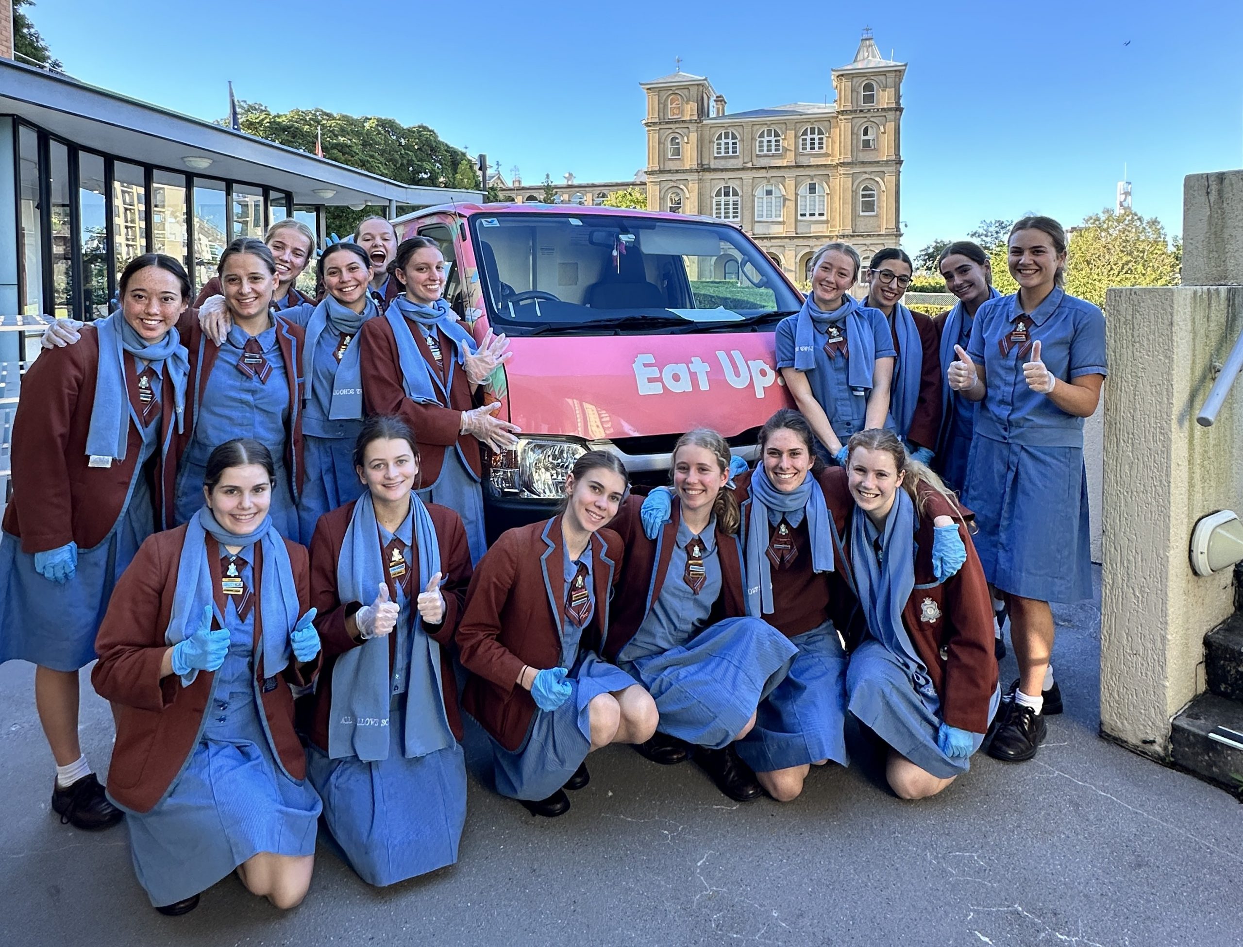 16 all Hallows' students rally around a catering donation van during their mission to feed the hungry